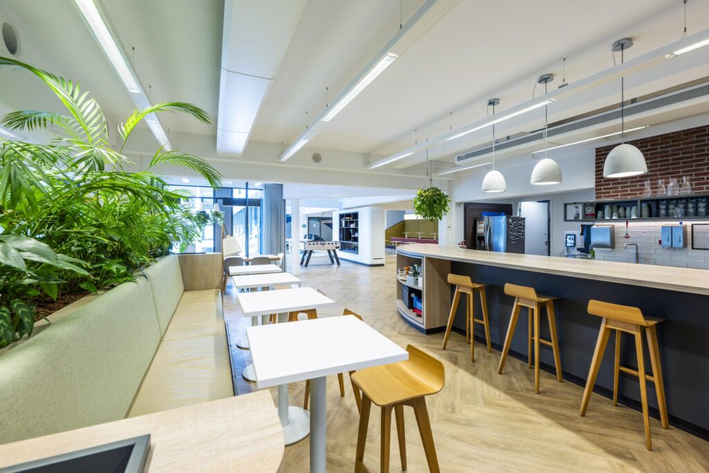 Modern office cafeteria on Mr. Treublaan with wooden furniture, hanging plants, and a coffee bar.